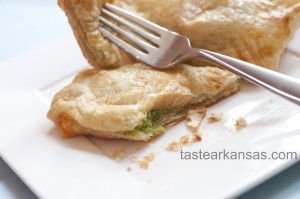 This picture shows a lightly browned, puff pastry packet that is filled with a warm mixture of avocado, cream cheese and salsa. The edges are brown and the pastry is buttery, flaky and delicious. A corner of the pastry is pierced on the end of a fork and the warm avocado is peaking out from the sliced corner.