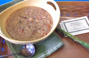 a delicious bowl of gumbo accented by sprigs of rice and a warm colored wooden tray