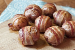 This image shows steamy tender red potatoes wrapped with crispy Petit Jean Bacon on a wooden cutting board, ready to eat.