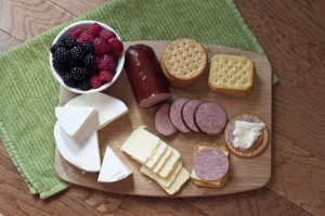This photo is a colorful example of a Cheese Board appetizer using Petit Jean Summer Sausage. On this cheese board is summer sausage, brie, extra sharp aged white cheddar, crackers and berries.