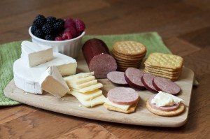 This photo is a colorful example of a Cheese Board appetizer using Petit Jean Summer Sausage. On this cheese board is summer sausage, brie, extra sharp aged white cheddar, crackers and berries.