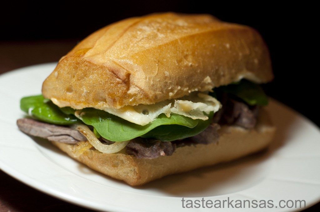 This image is of a steak sandiwch with provolone cheese, havarti cheese, spicy mayonnaise, caramelized onions, and spinach