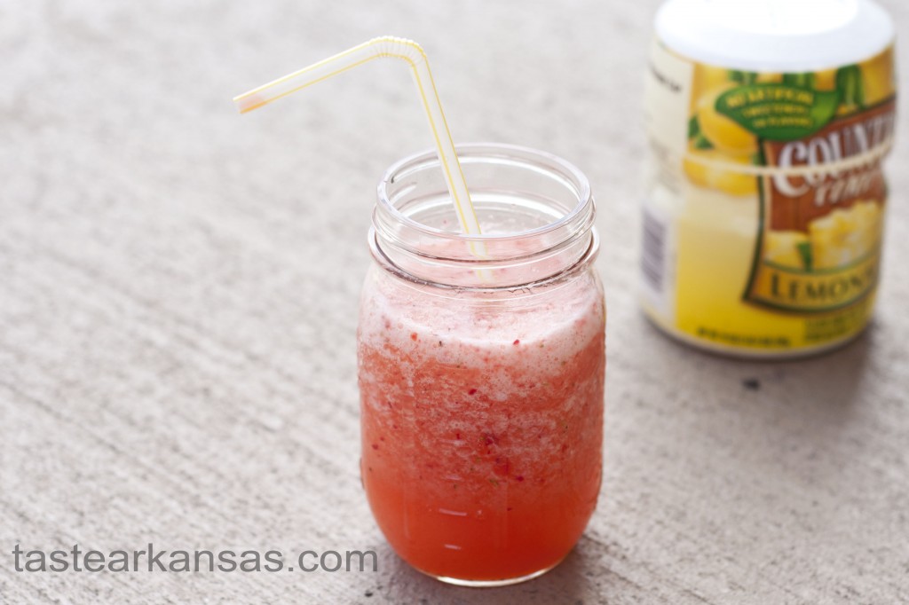 this photo is of strawberry lemonade slush in a mason jar with a straw and a container of countrytime lemonade in the background